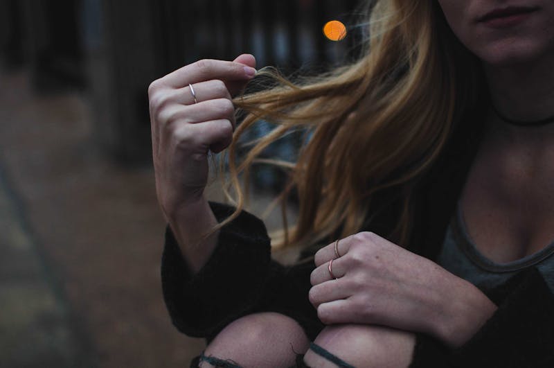 A young girl sitting playing with her hair and ripped jeans